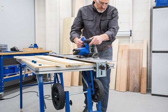 Woodworker using the Kreg ACS2000 Adaptive Cutting System to precisely cut a large sheet of plywood, demonstrating its stability and accuracy in action.