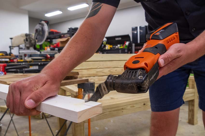 A craftsman using the Fein MultiMaster 700 FPM to precisely cut a piece of wood trim, demonstrating its ergonomic design and control during an in-use scenario.