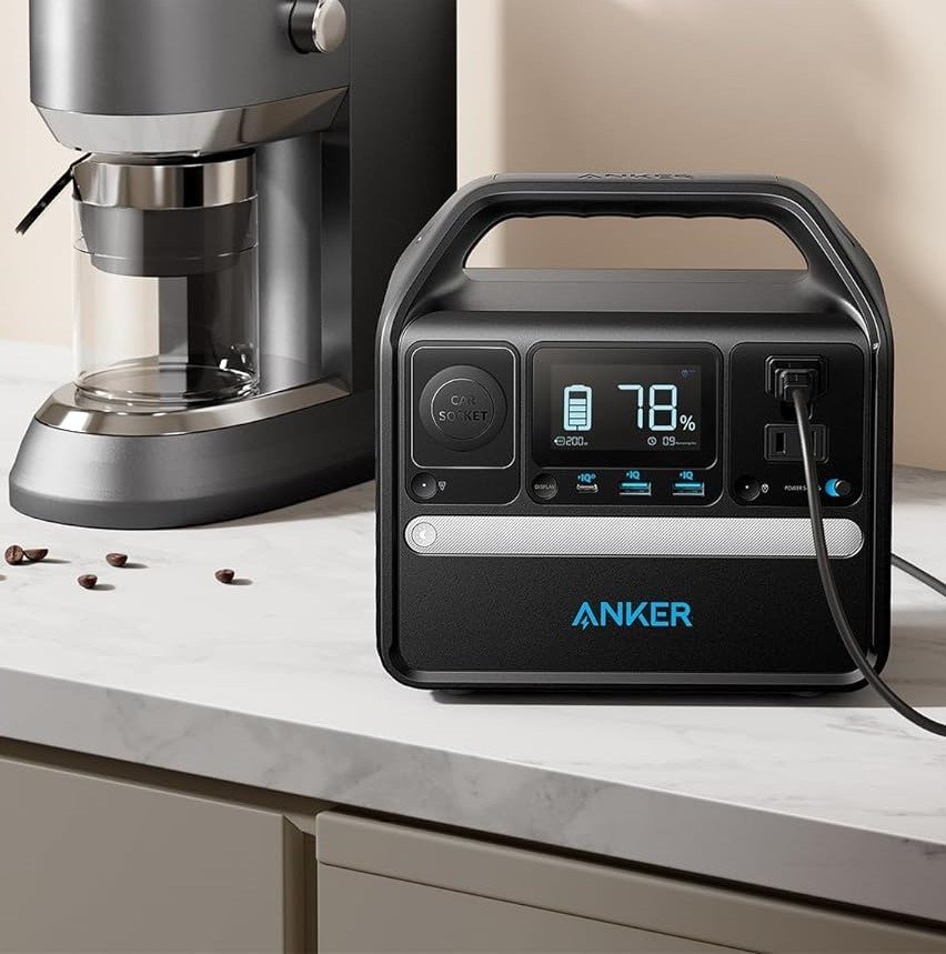 The Anker 521 Portable Power Station in action, powering a laptop and smartphone on a wooden desk, illustrating its practical use for remote work or creative tasks.