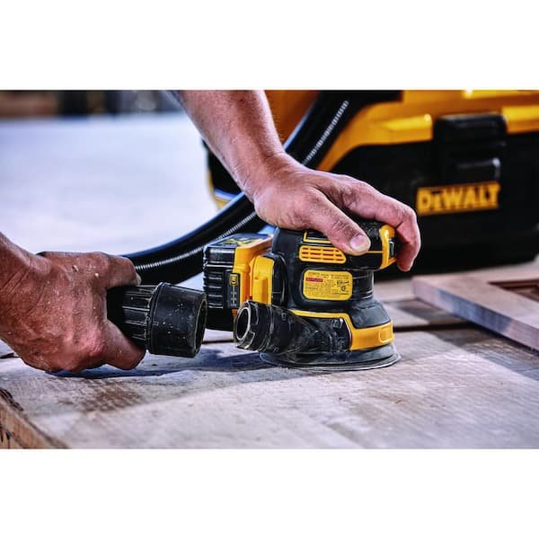DeWalt DCW210B 20V MAX XR Brushless 5 Random Orbital Sander in action, held by a user's hand, sanding a wooden surface to demonstrate its real-world application and ergonomic grip.