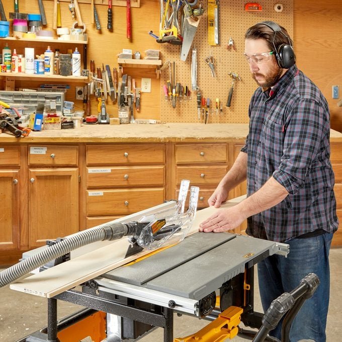 Woodworker precisely cutting a board with the DEWALT DWE7491RS 10-Inch Jobsite Table Saw, highlighting its rack and pinion fence system and ease of use in a workshop setting.
